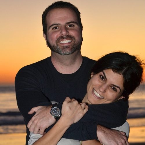 A man embracing a woman on the beach, with a sunset in the background.